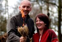 A man and woman laughing whilst holding a bundle of kindling which is alight