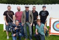 Seven people posing with two archery bows in front of target