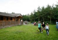 Children playing in a large grassy clearing behind a wooden lodge
