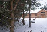 A wooden lodge in winter, with snow on the ground, roof and surrounding trees