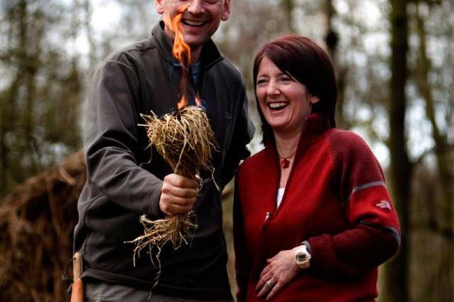 A man and woman laughing whilst holding a bundle of kindling which is alight